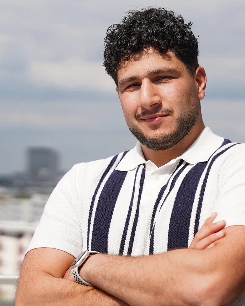 Karosch Gaedi mit verschränkten Armen, links im Bild die Hochhäuser der Stadt